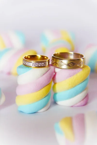 Złote obrączki ślubne na tle wielokolorowych marshmallows — Zdjęcie stockowe