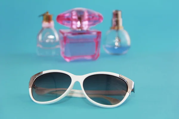 Gafas de sol en una montura de plástico blanco y frascos de perfume sobre fondo azul — Foto de Stock