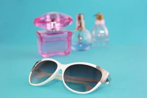 Sunglasses in a white plastic frame and perfume bottles on a blue background — Stock Photo, Image