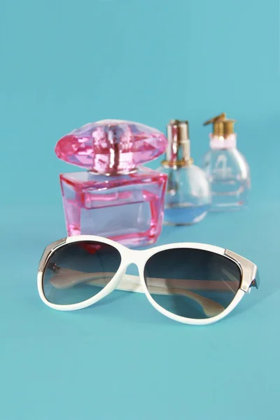 Sunglasses in a white plastic frame and perfume bottles on a blue background — Stock Photo, Image