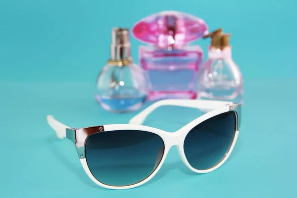 Okulary przeciwsłoneczne w białej plastikowej ramie i butelki perfum na niebieskim tle — Zdjęcie stockowe