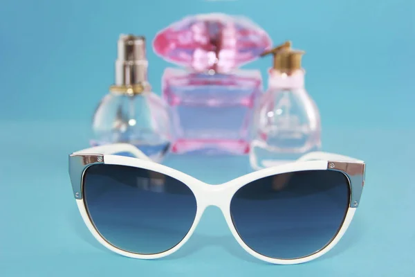 Sunglasses in a white plastic frame and perfume bottles on a blue background — Stock Photo, Image