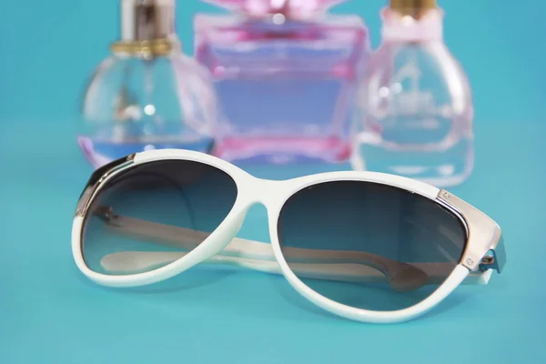 Okulary przeciwsłoneczne w białej plastikowej ramie i butelki perfum na niebieskim tle — Zdjęcie stockowe