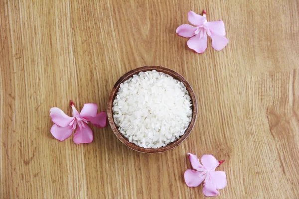 Белый натуральный рис в коричневой деревянной тарелке и декоративные розовые цветы на желтом фоне — стоковое фото
