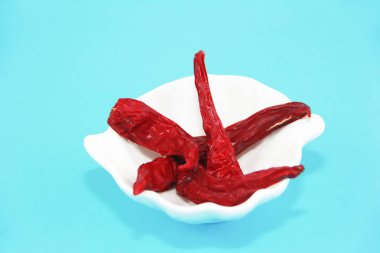 mavi bir arka plan üzerinde beyaz tabakta kırmızı baharatlı kurutulmuş küçük biber