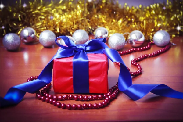 Червона подарункова коробка з синім бантом на фоні різдвяних іграшок на новорічне свято — стокове фото
