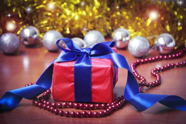 Червона подарункова коробка з синім бантом на фоні різдвяних іграшок на новорічне свято — стокове фото