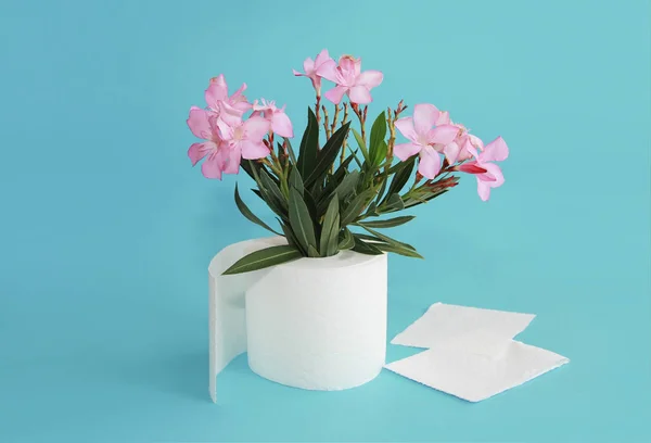 Rollo de papel higiénico y flores rosadas sobre un fondo azul — Foto de Stock