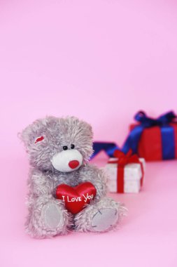 elinde kırmızı bir kalp ve hediyeler ile bir kutu ile oyuncak oyuncak kabarık ayı