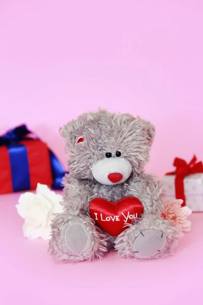 toy teddy fluffy bear with a red heart in hands and a boxes with gifts