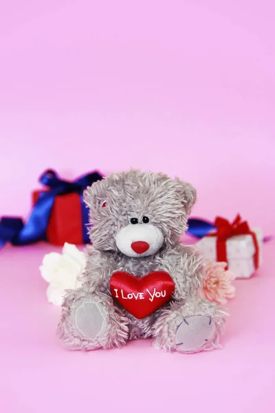 Juguete peluche oso esponjoso con un corazón rojo en las manos y una caja con regalos — Foto de Stock