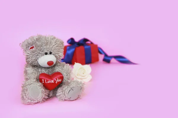 Juguete peluche oso esponjoso con un corazón rojo en las manos y una caja con regalos — Foto de Stock