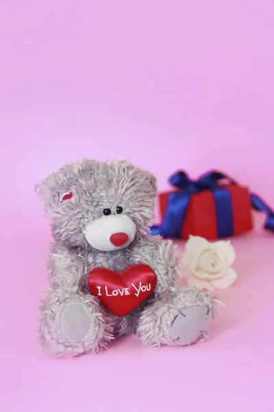 Jouet ours pelucheux en peluche avec un coeur rouge dans les mains et une boîte avec des cadeaux — Photo