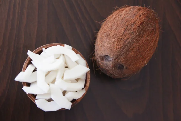 Fruta de coco marrom e fatias de coco branco natural em uma placa de madeira — Fotografia de Stock