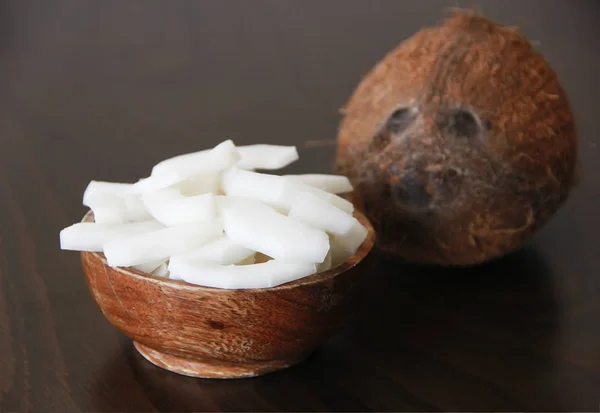 Noix de coco brune et tranches de noix de coco blanche naturelle dans une assiette en bois — Photo