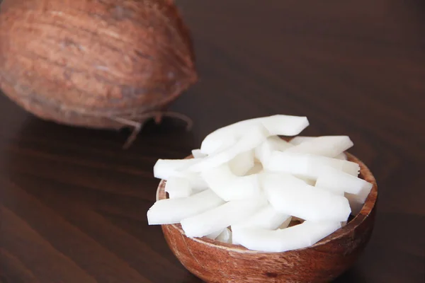 Noix de coco brune et tranches de noix de coco blanche naturelle dans une assiette en bois — Photo