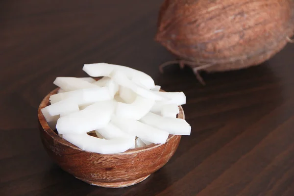 Noix de coco brune et tranches de noix de coco blanche naturelle dans une assiette en bois — Photo