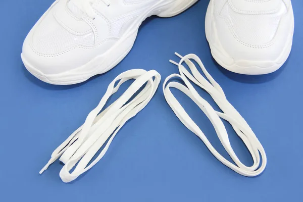 Zapatillas deportivas y cordones blancos sobre fondo azul — Foto de Stock