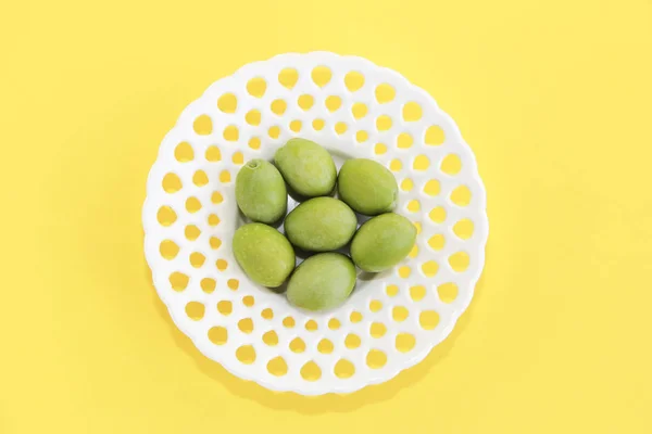 Olives fraîches naturelles vertes dans une assiette décorative blanche sur fond jaune — Photo