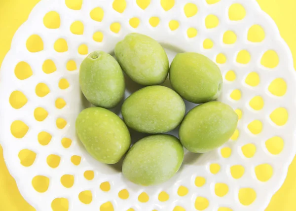 Zelená přírodní čerstvé olivy v bílé dekorativní talíř na žlutém pozadí — Stock fotografie
