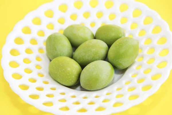 Olives fraîches naturelles vertes dans une assiette décorative blanche sur fond jaune — Photo