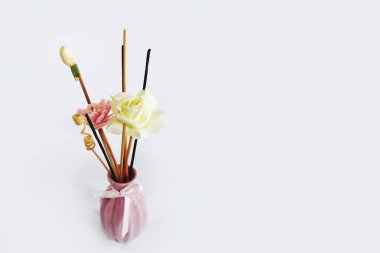 Pembe seramik vazoda aromaterapi çubukları ve dekoratif yapay çiçekler.