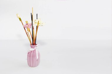 Pembe seramik vazoda aromaterapi çubukları ve dekoratif yapay çiçekler.