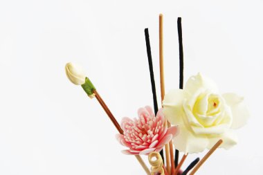 Pembe seramik vazoda aromaterapi çubukları ve dekoratif yapay çiçekler.