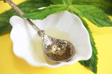 Süslü kaşık ve yeşil nane yapraklarında sarı aromatik yağ.