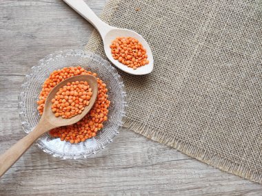 Dekoratif bir tabakta kurumuş küçük kırmızı mercimek ve ahşap bir arka planda tahta kaşıklar.