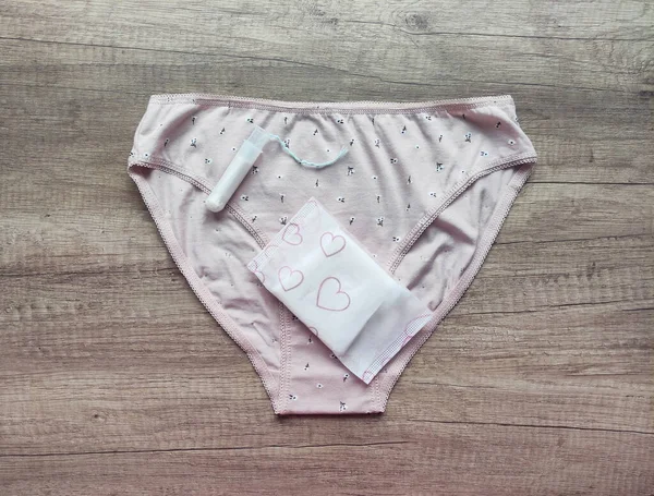 Ahşap arka planda kadın iç çamaşırı, hijyenik pedler ve tamponlar.