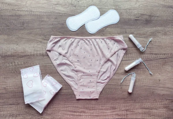 Ahşap arka planda kadın iç çamaşırı, hijyenik pedler ve tamponlar.