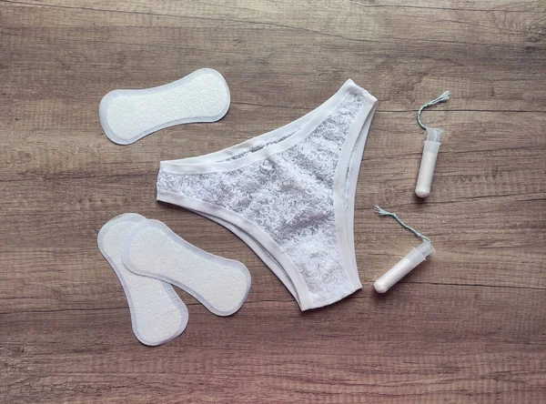Ahşap arka planda kadın iç çamaşırı, hijyenik pedler ve tamponlar.