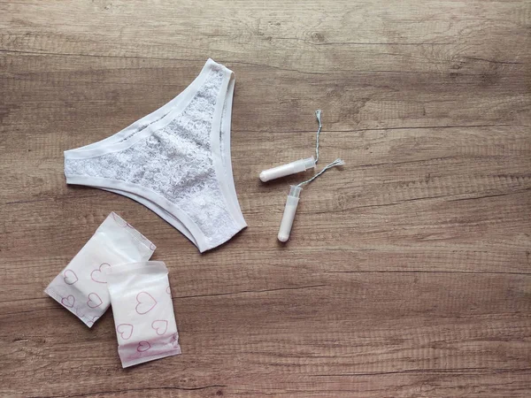 Ahşap arka planda kadın iç çamaşırı, hijyenik pedler ve tamponlar.