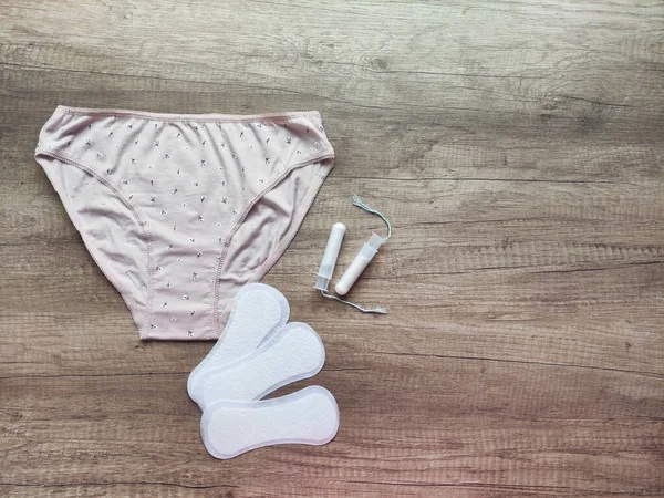 Ahşap arka planda kadın iç çamaşırı, hijyenik pedler ve tamponlar.