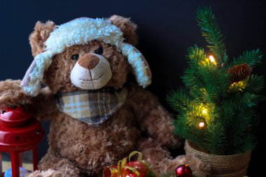 Sevimli oyuncak ayı bir pençe üzerinde siyah bir arka plan üzerinde kırmızı bir fener tutarak. Çerçevede, süs eşyaları ile küçük bir Noel ağacı görebilirsiniz.