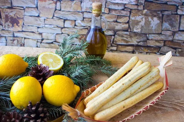 Палочки (гриссини) на плетеной тарелке, лимоны и оливковое масло — стоковое фото
