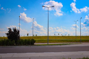 Otoyoldaki boş otopark. Küçük tepelerin ve bulutlu gökyüzünün arka planında fenerler