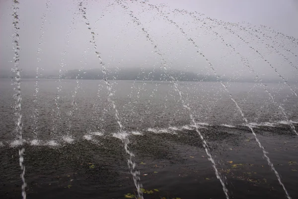 噴水のジェットは多くのスプラッシュを形成する湖に落ちます 反対側の海岸は 湖が霧で覆われているので バックグラウンドではほとんど見えません — ストック写真