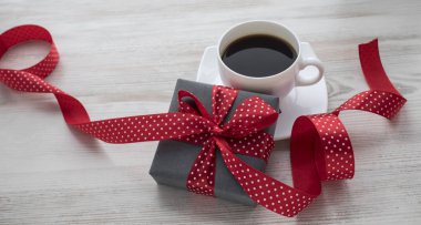 Hediye veya mevcut kutusunda kırmızı kurdele ve üzerinde bir ahşap beyaz backgraund fincan kahve ile kraft kağıt sarılı