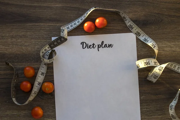 Diet plan, menu or program, measuring tape and diet food fresh arugula and cherry tomatoes on a dark wooden background, weight loss and detoxification concept, top view