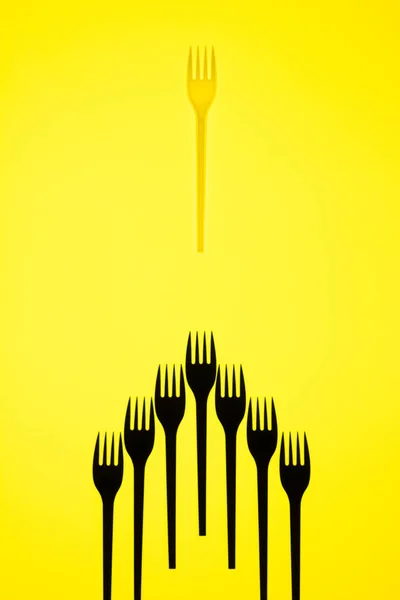 Sarı arka plan üzerinde yedi siyah çatal ve bir beyaz çataldan oluşan yüksek kontrastlı natürmortgörünümü