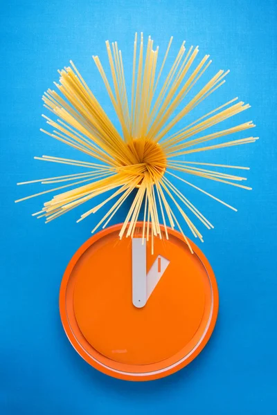 Set of spaghetti next to orange kitchen clock — Stock Photo, Image