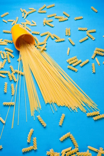 Spaghetti and macaroni scattered asymmetrically on a blue surface — Stock Photo, Image
