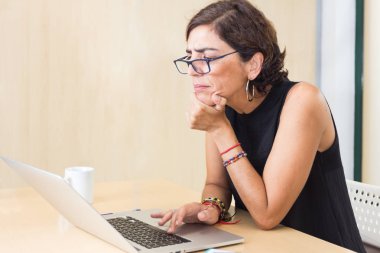 Yarı düşmüş gözlüklü kadın dizüstü bilgisayarının ekranına garip bir şekilde bakıyor.