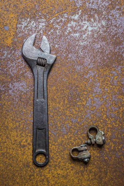 Wrench and battery terminals on rusty steel plate