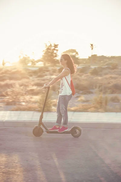 Gün batımında elektrikli scooter'a binen kadın