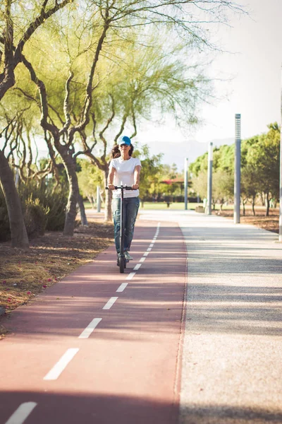 Kadın, yırtık kot giymiş, bisiklet şeritli tarafından elektrikli tekme scooter sürme