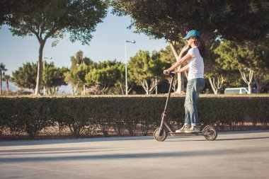 Kadın, kırık kot giymiş, elektrikli tekme scooter sürme
