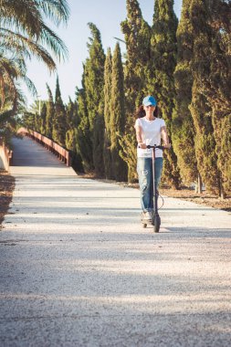 Kadın, kırık kot giymiş, elektrikli tekme scooter sürme
